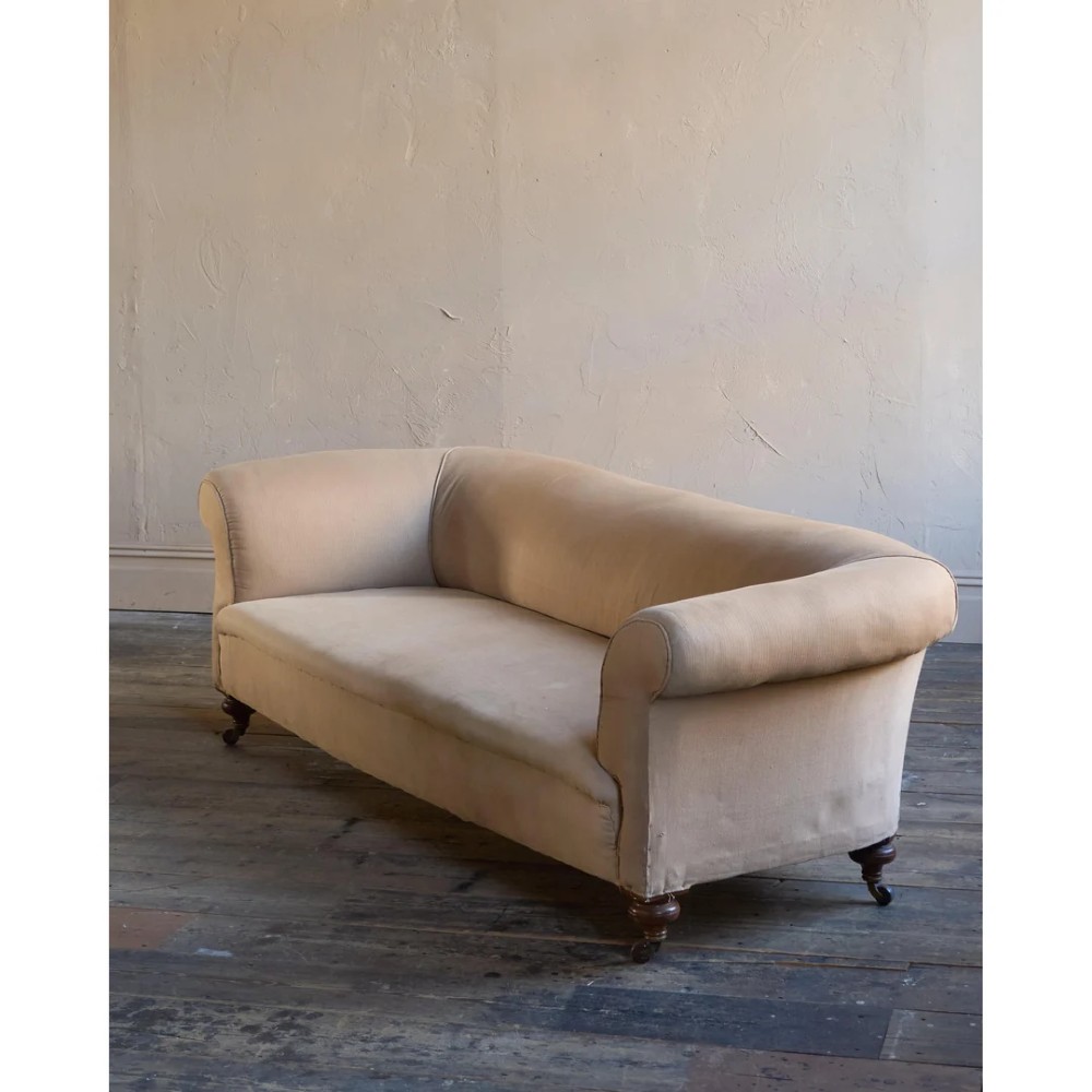 A 19th-century Chesterfield sofa upholstered in neutral beige calico fabric featuring rolled arms and turned wooden legs on brass castors. View III