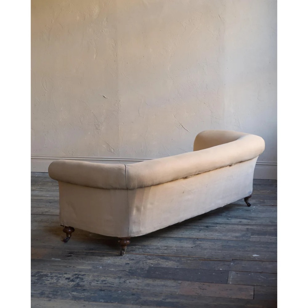 A 19th-century Chesterfield sofa upholstered in neutral beige calico fabric featuring rolled arms and turned wooden legs on brass castors. View IV