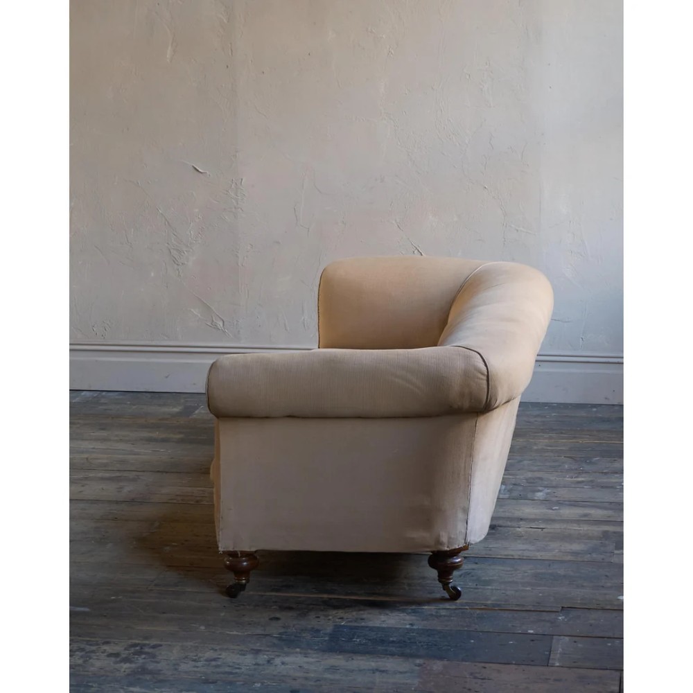 A 19th-century Chesterfield sofa upholstered in neutral beige calico fabric featuring rolled arms and turned wooden legs on brass castors. View VI