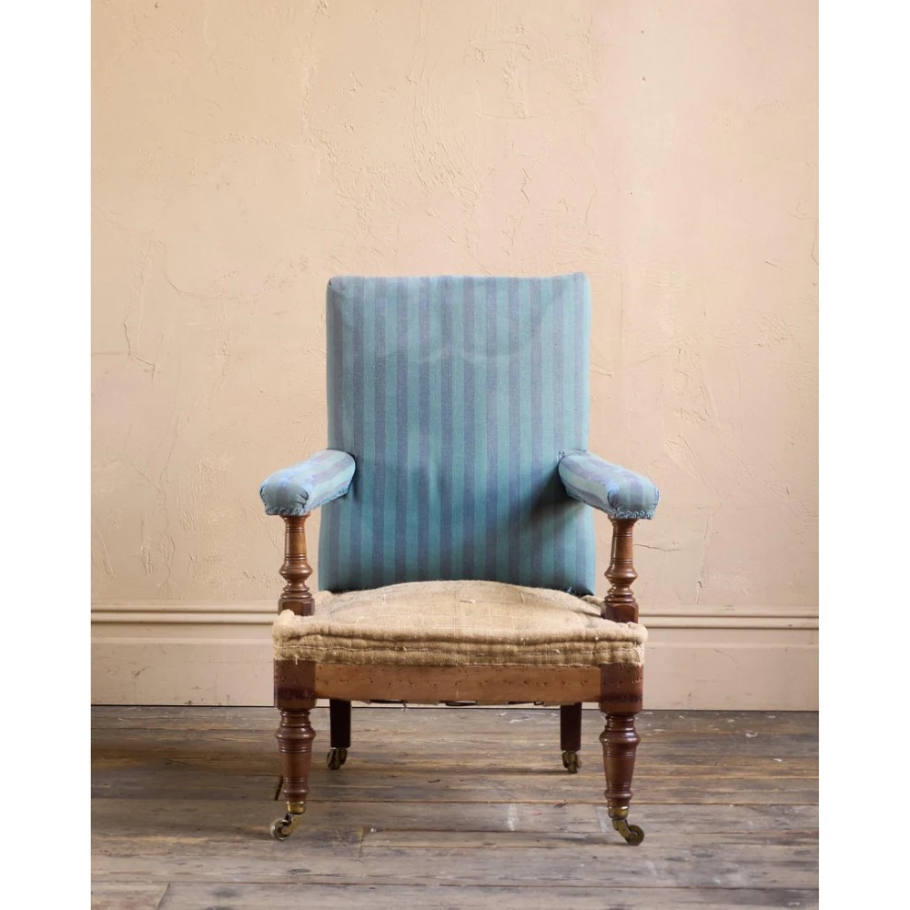 A Victorian mahogany open armchair with turned front legs, brass castors, open padded arms, and blue striped fabric upholstery. View III