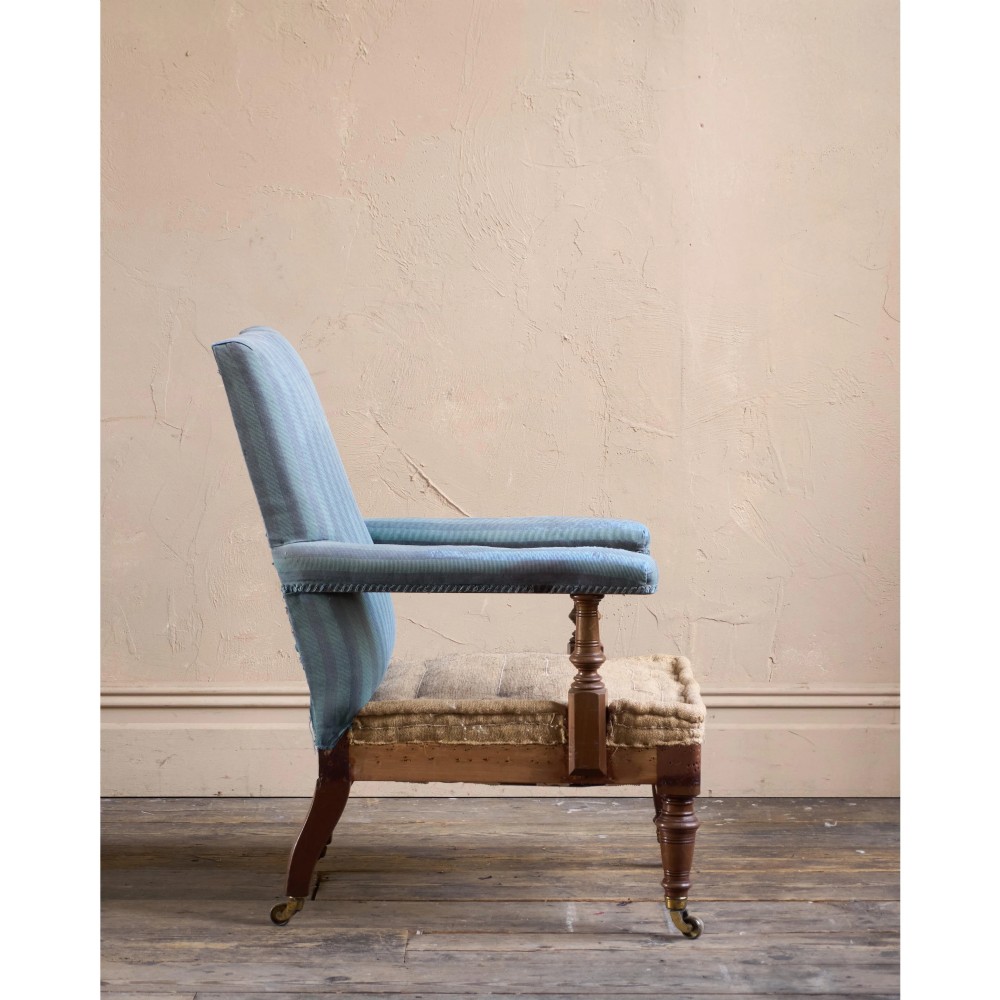 A Victorian mahogany open armchair with turned front legs, brass castors, open padded arms, and blue striped fabric upholstery. View IV
