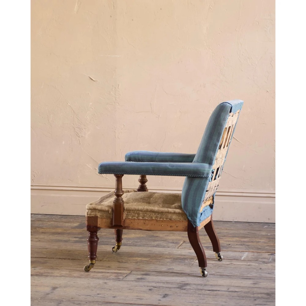 A Victorian mahogany open armchair with turned front legs, brass castors, open padded arms, and blue striped fabric upholstery. View V