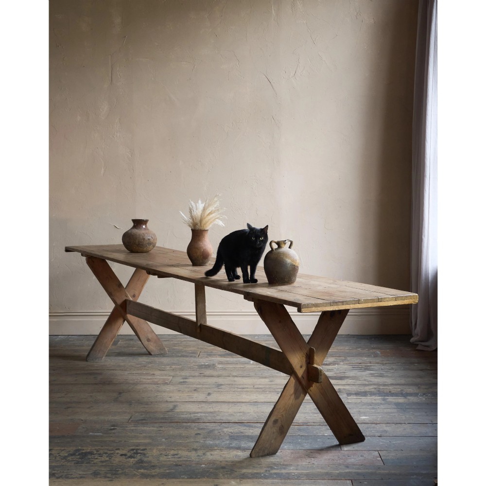 A long, narrow rustic wooden dining table featuring a thick plank top supported by X-frame trestle legs and a longitudinal stretcher. View II