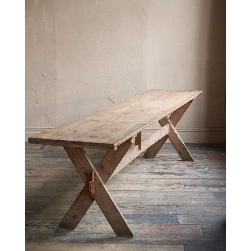 A long, narrow rustic wooden dining table featuring a thick plank top supported by X-frame trestle legs and a longitudinal stretcher. View III