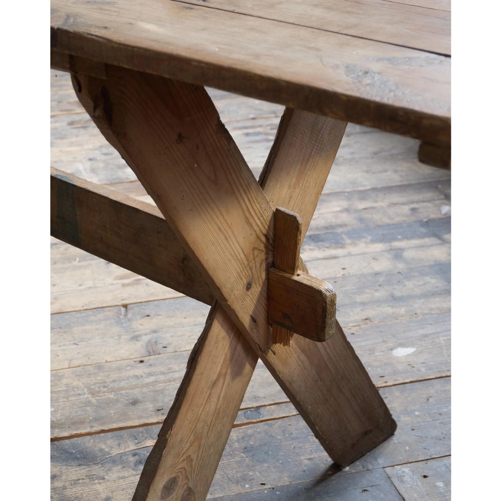 A long, narrow rustic wooden dining table featuring a thick plank top supported by X-frame trestle legs and a longitudinal stretcher. View V