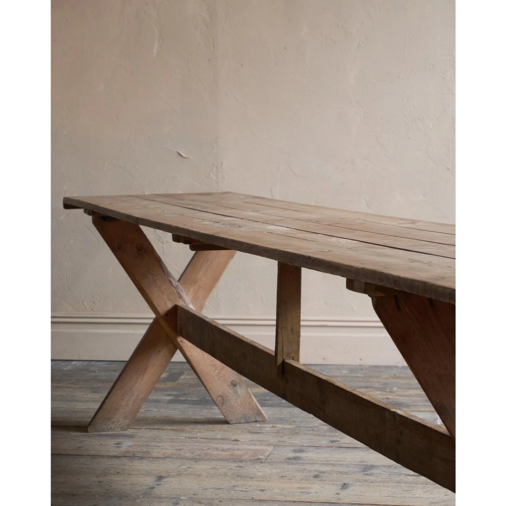 A long, narrow rustic wooden dining table featuring a thick plank top supported by X-frame trestle legs and a longitudinal stretcher. View VI