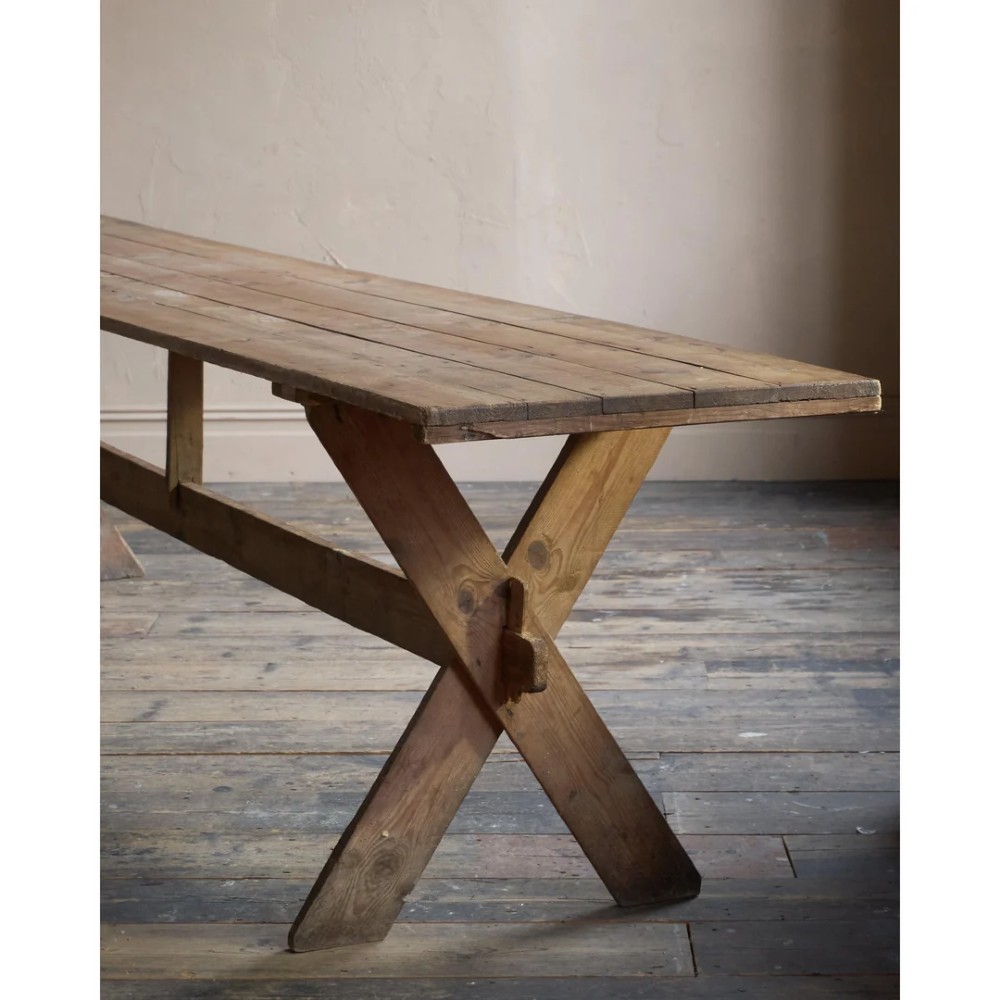 A long, narrow rustic wooden dining table featuring a thick plank top supported by X-frame trestle legs and a longitudinal stretcher. View VII