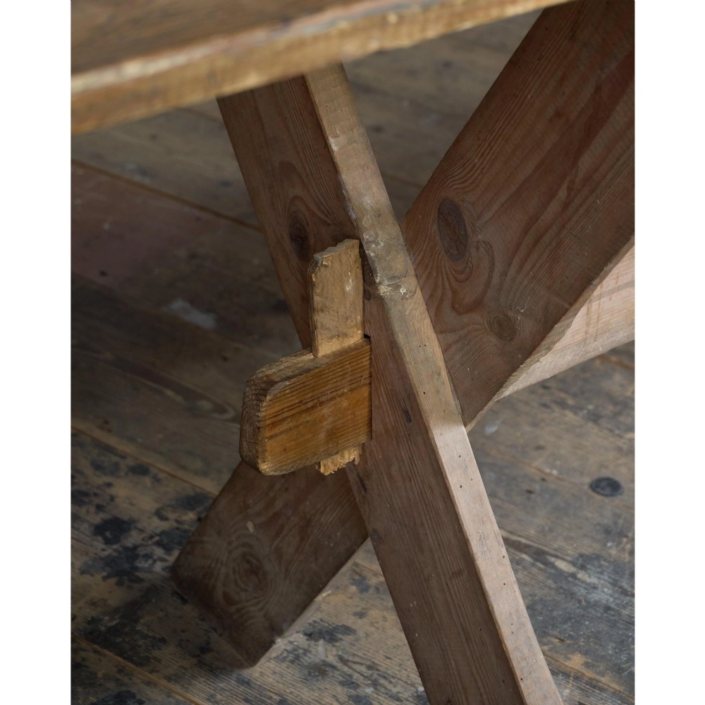 A long, narrow rustic wooden dining table featuring a thick plank top supported by X-frame trestle legs and a longitudinal stretcher. View XII