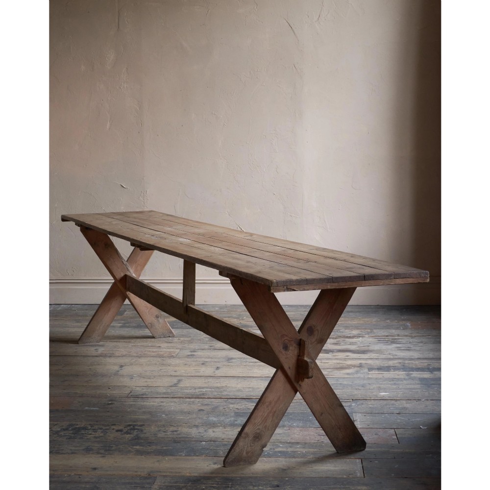 A long, narrow rustic wooden dining table featuring a thick plank top supported by X-frame trestle legs and a longitudinal stretcher. View XIII