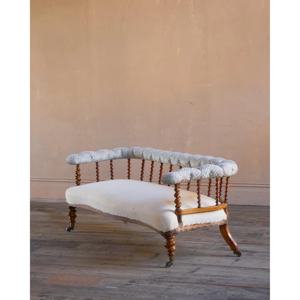 A nineteenth-century salon sofa featuring a curved button-upholstered crest rail supported by turned spindles, a cream padded seat, and turned mahogany legs on brass castors.