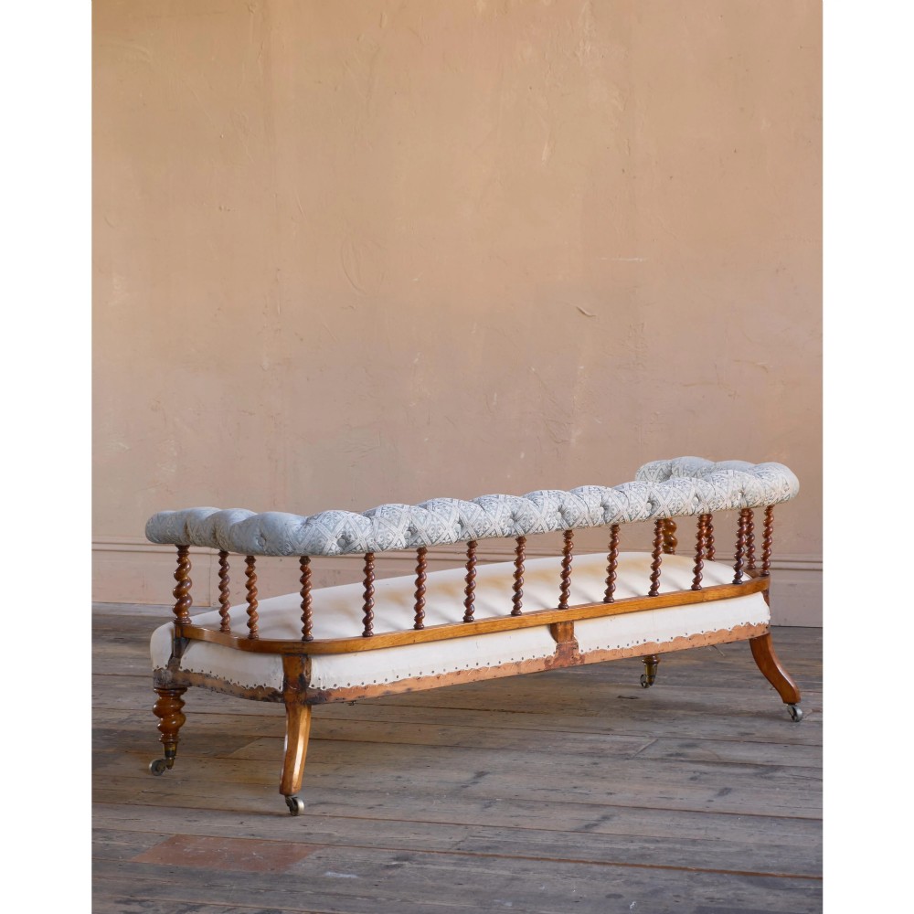 A nineteenth-century salon sofa featuring a curved button-upholstered crest rail supported by turned spindles, a cream padded seat, and turned mahogany legs on brass castors. View II