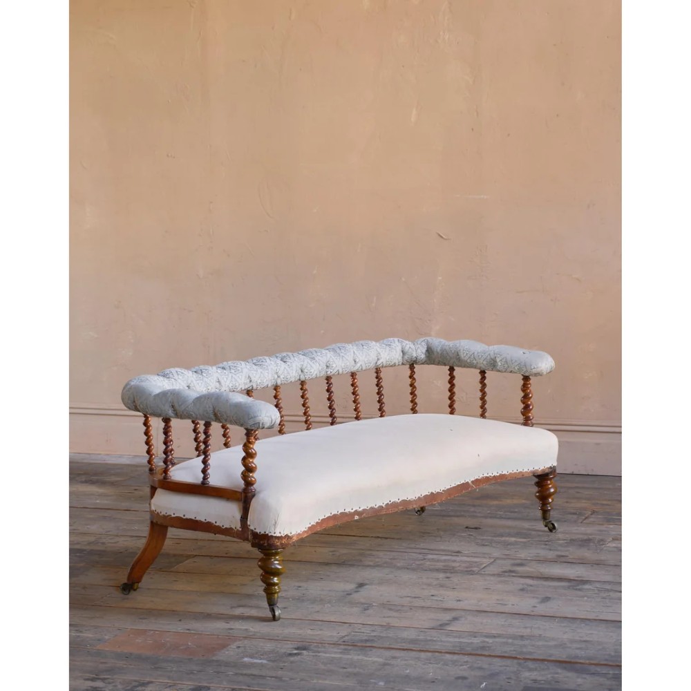 A nineteenth-century salon sofa featuring a curved button-upholstered crest rail supported by turned spindles, a cream padded seat, and turned mahogany legs on brass castors. View III