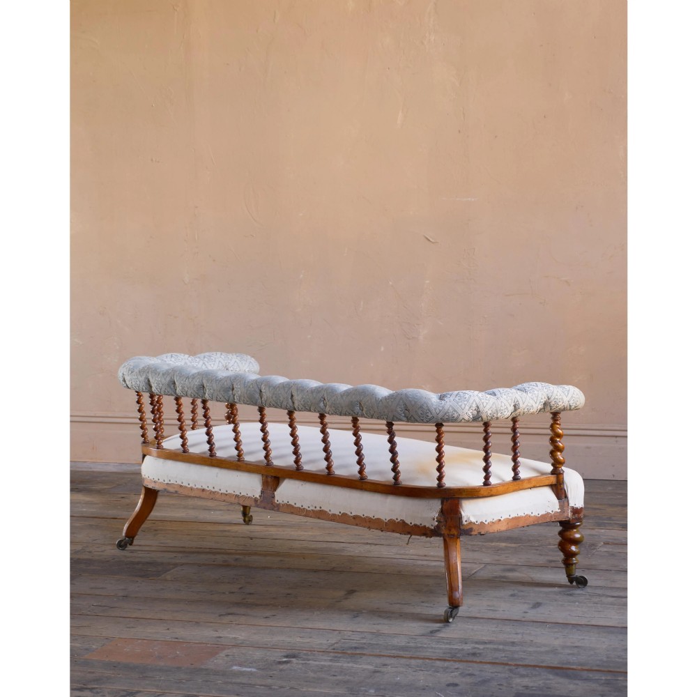 A nineteenth-century salon sofa featuring a curved button-upholstered crest rail supported by turned spindles, a cream padded seat, and turned mahogany legs on brass castors. View IV