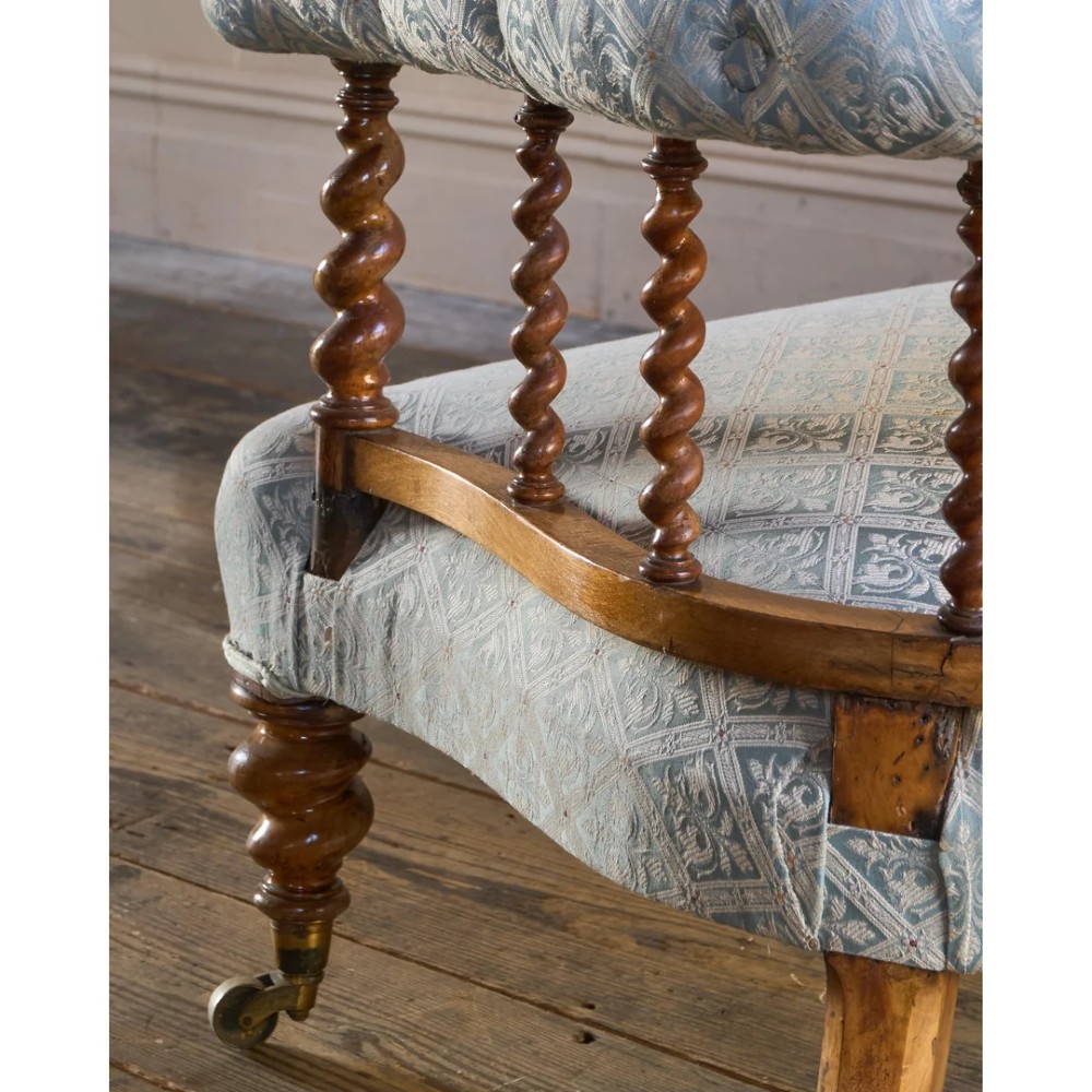 A nineteenth-century salon sofa featuring a curved button-upholstered crest rail supported by turned spindles, a cream padded seat, and turned mahogany legs on brass castors. View VI