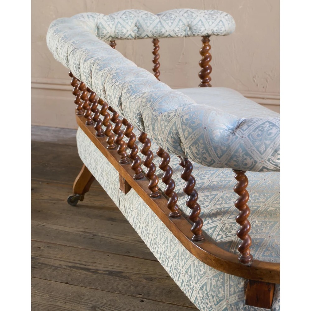 A nineteenth-century salon sofa featuring a curved button-upholstered crest rail supported by turned spindles, a cream padded seat, and turned mahogany legs on brass castors. View VII