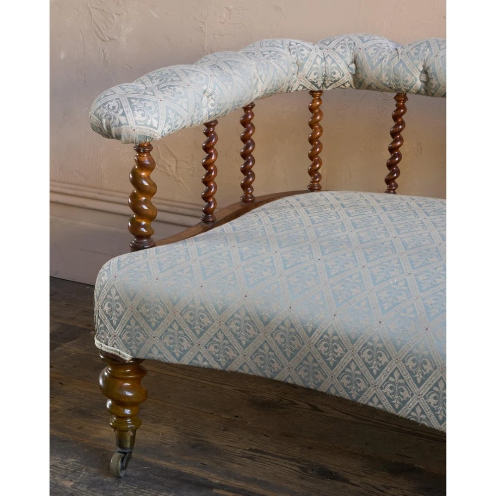 A nineteenth-century salon sofa featuring a curved button-upholstered crest rail supported by turned spindles, a cream padded seat, and turned mahogany legs on brass castors. View VIII