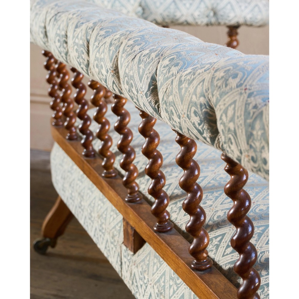 A nineteenth-century salon sofa featuring a curved button-upholstered crest rail supported by turned spindles, a cream padded seat, and turned mahogany legs on brass castors. View IX