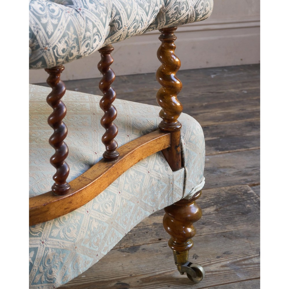 A nineteenth-century salon sofa featuring a curved button-upholstered crest rail supported by turned spindles, a cream padded seat, and turned mahogany legs on brass castors. View X