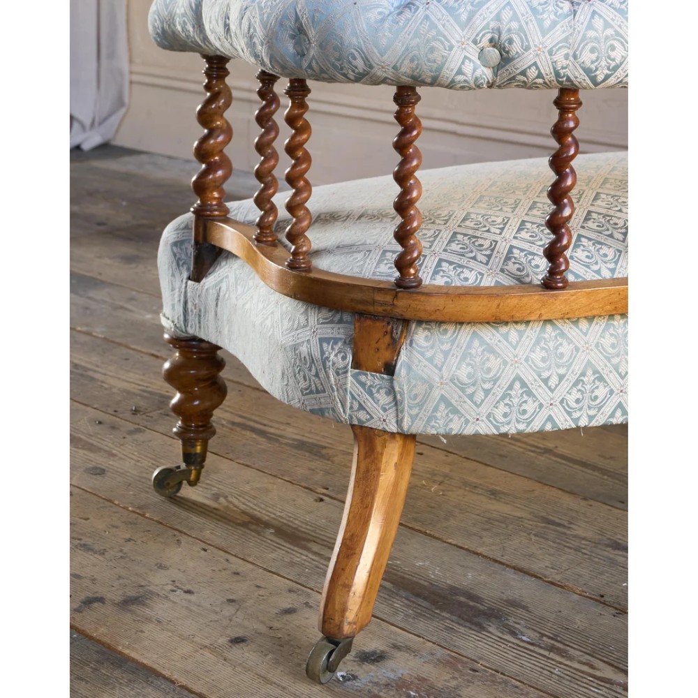 A nineteenth-century salon sofa featuring a curved button-upholstered crest rail supported by turned spindles, a cream padded seat, and turned mahogany legs on brass castors. View XI