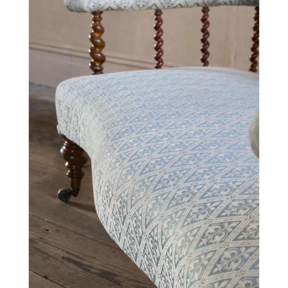A nineteenth-century salon sofa featuring a curved button-upholstered crest rail supported by turned spindles, a cream padded seat, and turned mahogany legs on brass castors. View XII