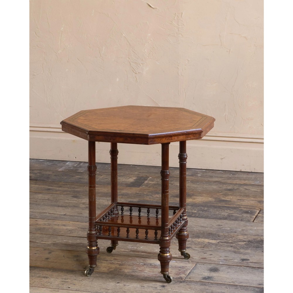 An octagonal Victorian side table featuring an amboyna wood veneer top with gilt borders, turned legs, a lower shelf with a spindle gallery, and brass castors. View II