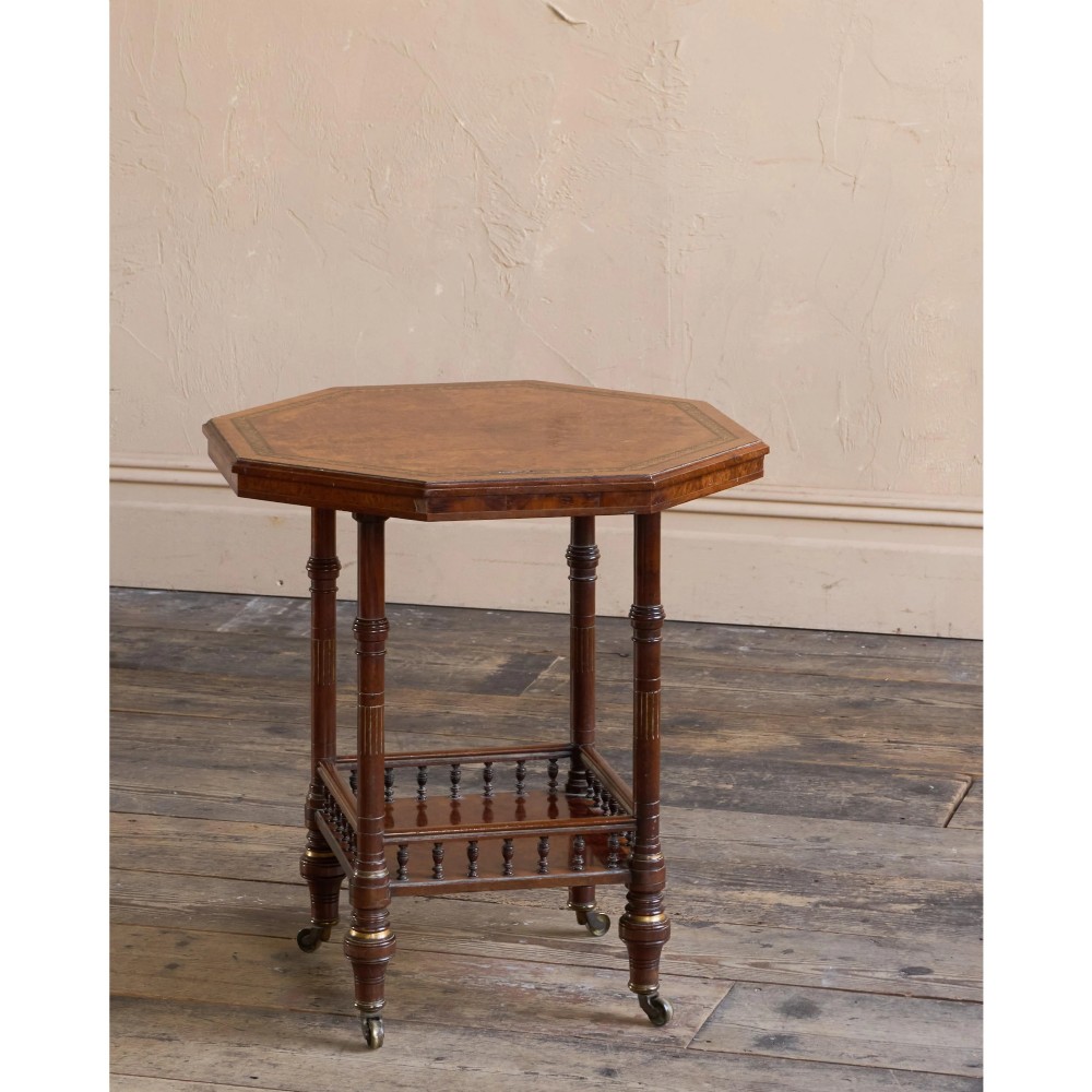 An octagonal Victorian side table featuring an amboyna wood veneer top with gilt borders, turned legs, a lower shelf with a spindle gallery, and brass castors. View III
