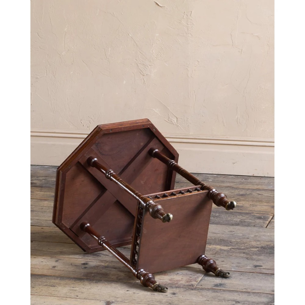 An octagonal Victorian side table featuring an amboyna wood veneer top with gilt borders, turned legs, a lower shelf with a spindle gallery, and brass castors. View V