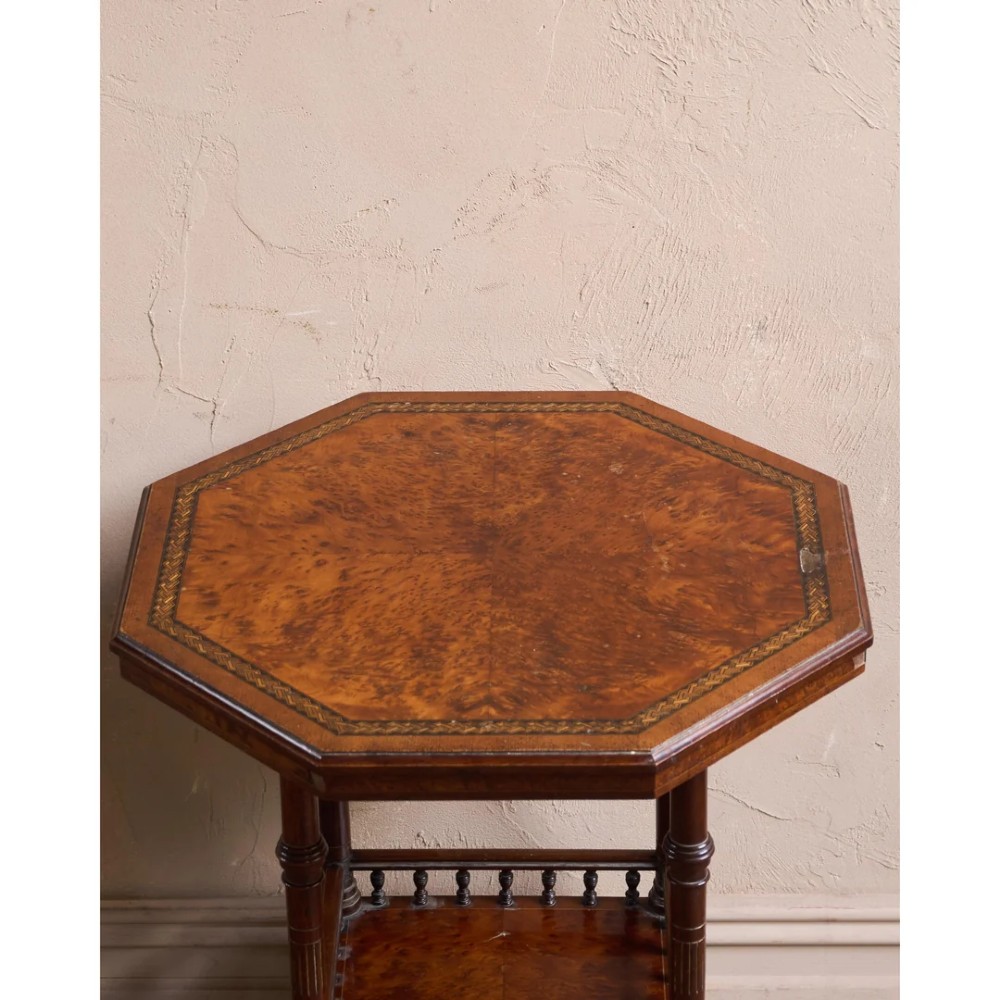 An octagonal Victorian side table featuring an amboyna wood veneer top with gilt borders, turned legs, a lower shelf with a spindle gallery, and brass castors. View VI
