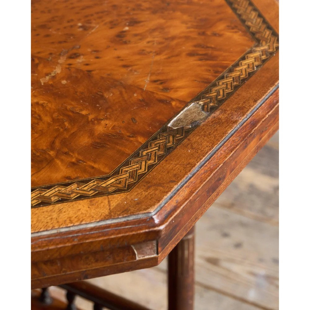 An octagonal Victorian side table featuring an amboyna wood veneer top with gilt borders, turned legs, a lower shelf with a spindle gallery, and brass castors. View VIII