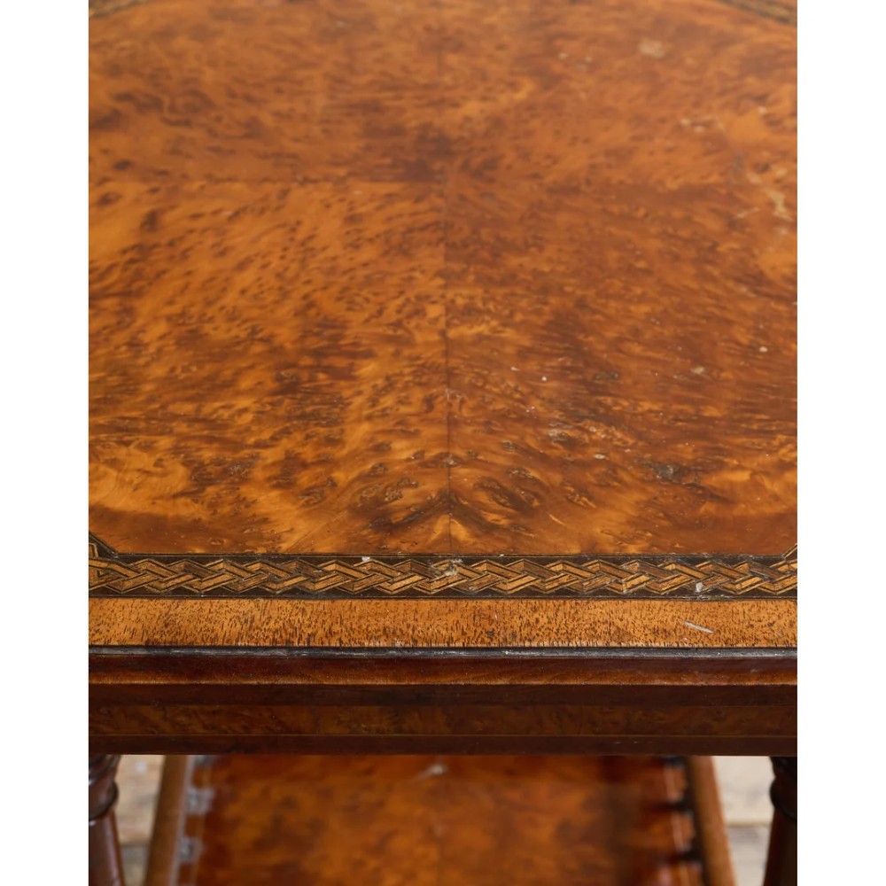 An octagonal Victorian side table featuring an amboyna wood veneer top with gilt borders, turned legs, a lower shelf with a spindle gallery, and brass castors. View X