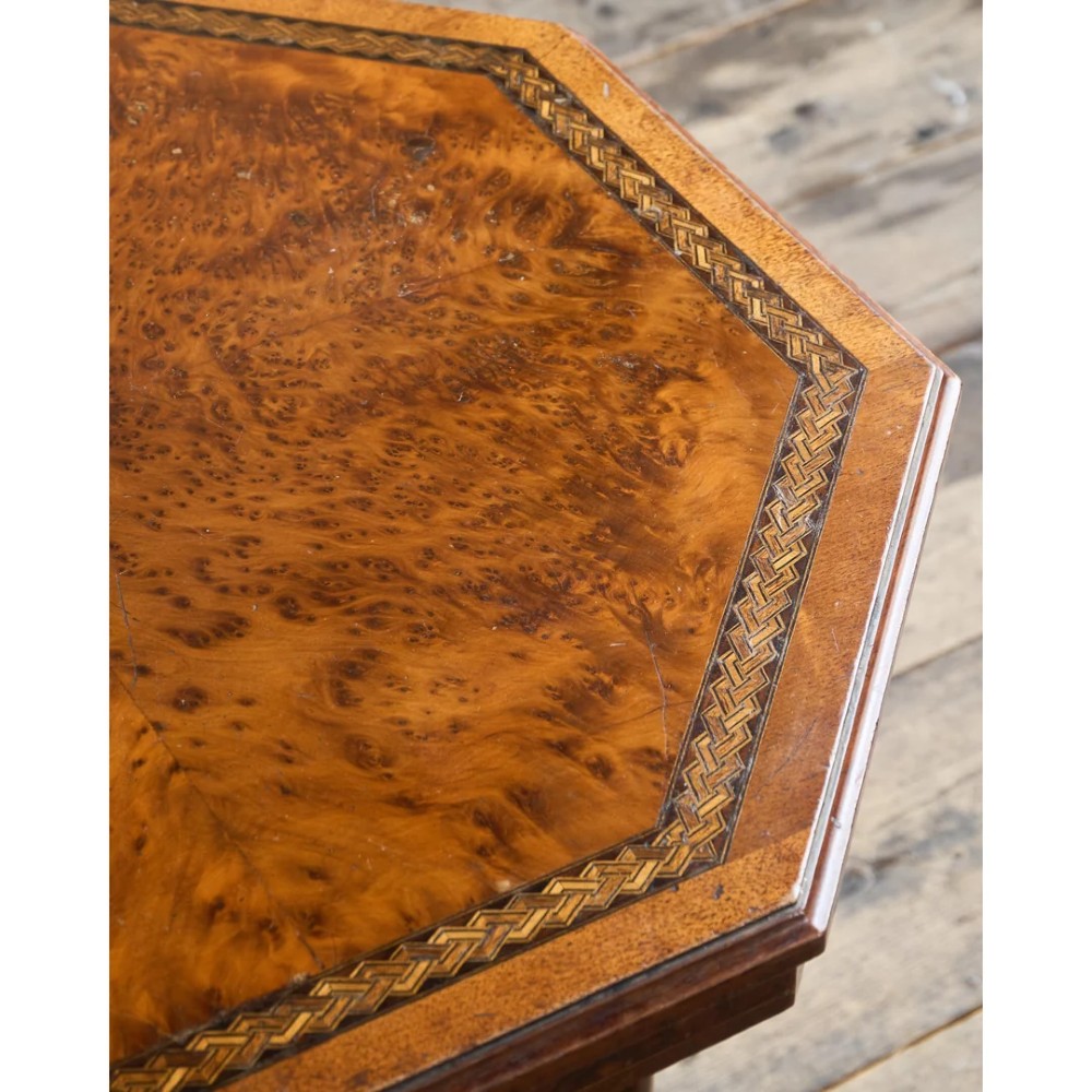 An octagonal Victorian side table featuring an amboyna wood veneer top with gilt borders, turned legs, a lower shelf with a spindle gallery, and brass castors. View XII