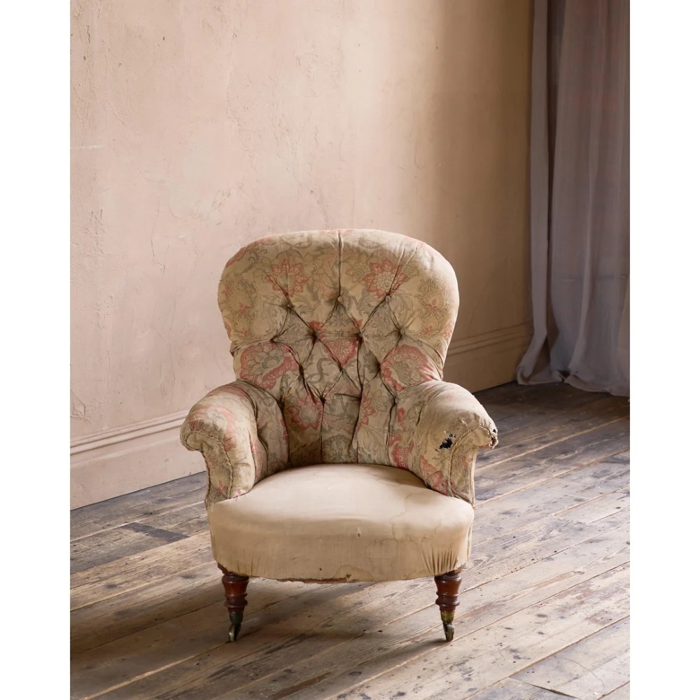 An antique Victorian spoon-back armchair with deep button tufting, worn floral upholstery, turned mahogany front legs, and brass castors. View III