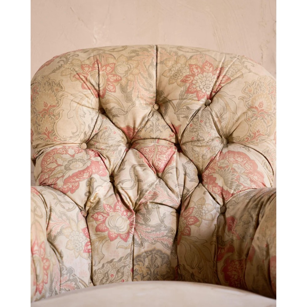 An antique Victorian spoon-back armchair with deep button tufting, worn floral upholstery, turned mahogany front legs, and brass castors. View VI