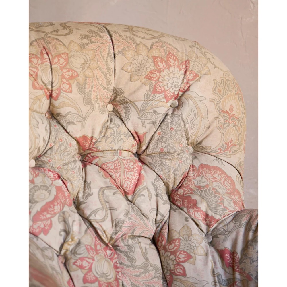 An antique Victorian spoon-back armchair with deep button tufting, worn floral upholstery, turned mahogany front legs, and brass castors. View VII