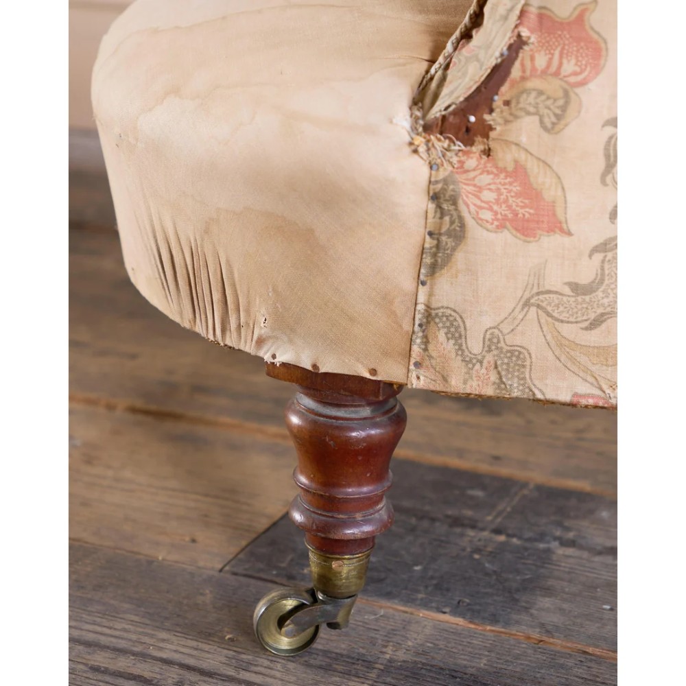An antique Victorian spoon-back armchair with deep button tufting, worn floral upholstery, turned mahogany front legs, and brass castors. View VIII