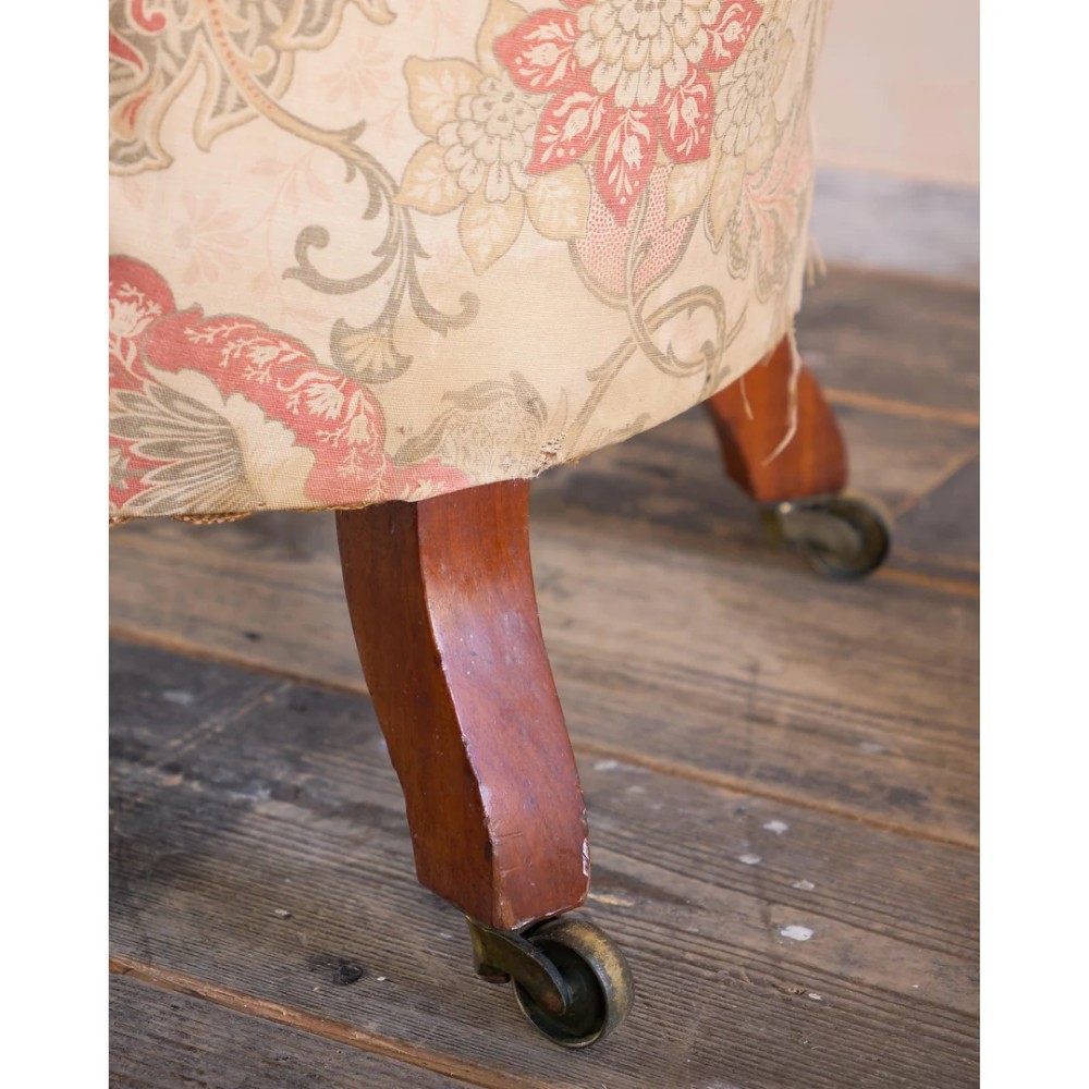 An antique Victorian spoon-back armchair with deep button tufting, worn floral upholstery, turned mahogany front legs, and brass castors. View IX