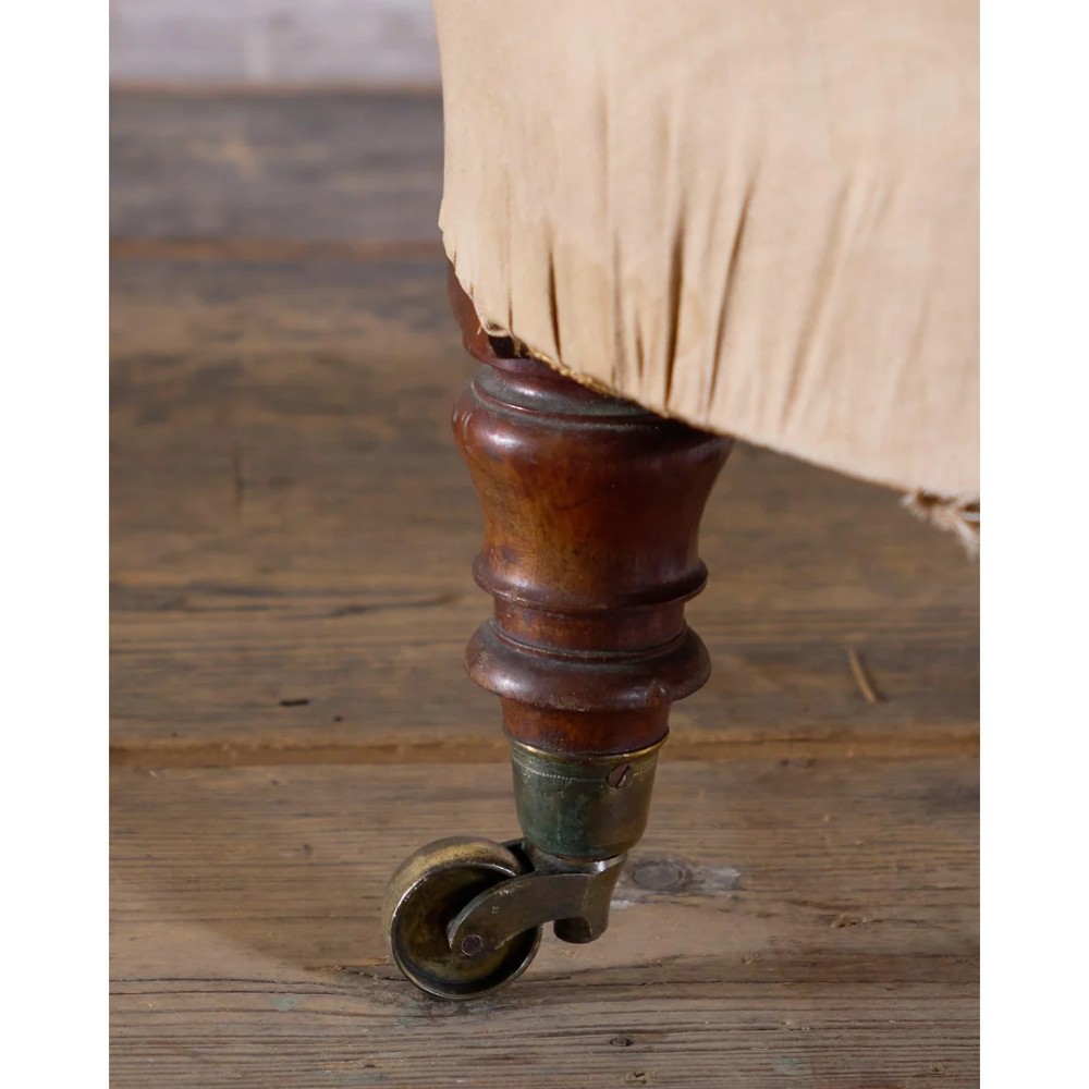 An antique Victorian spoon-back armchair with deep button tufting, worn floral upholstery, turned mahogany front legs, and brass castors. View X