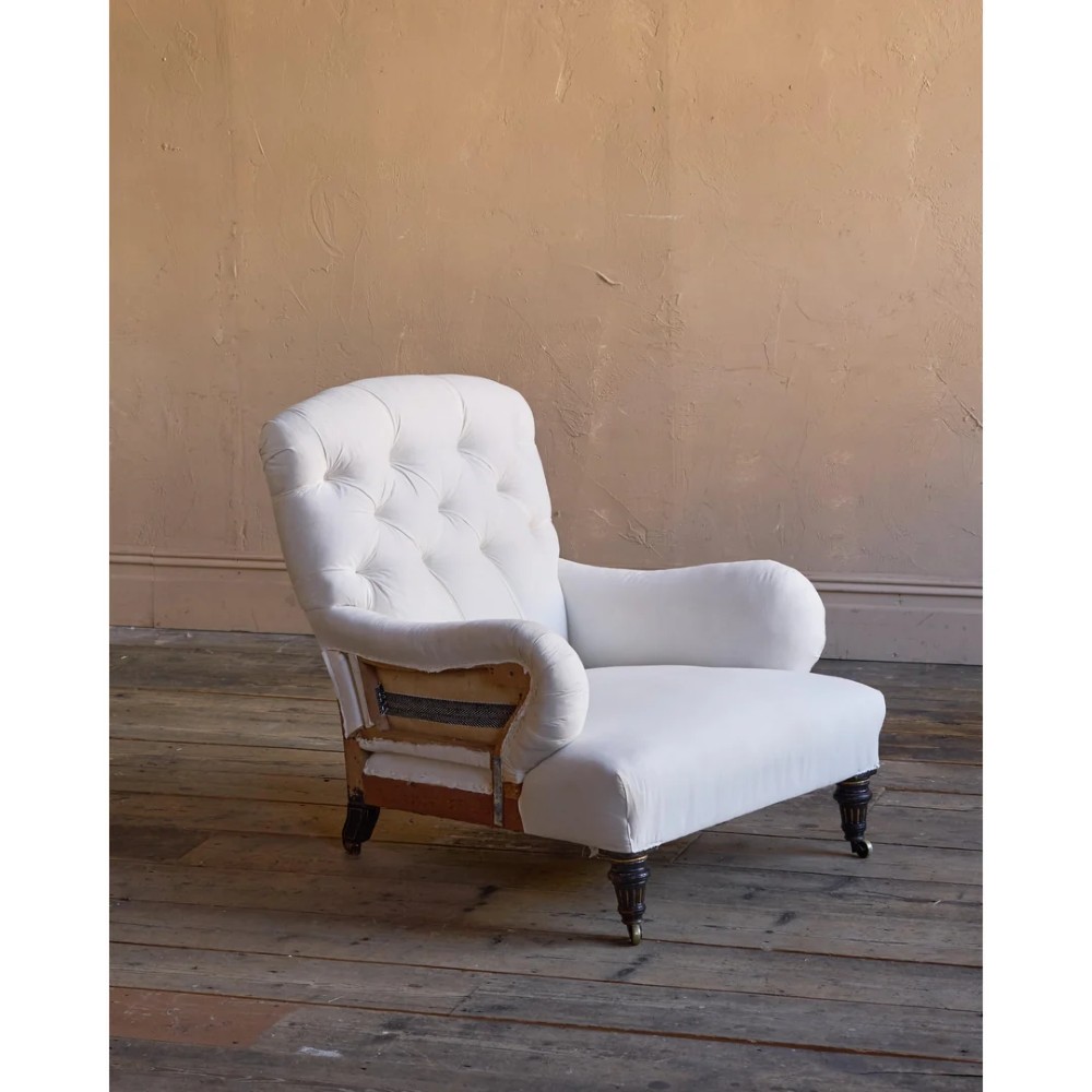 A deep-seated Howard style armchair upholstered in cream calico fabric with a button-tufted backrest and turned wooden legs on brass castors. View II