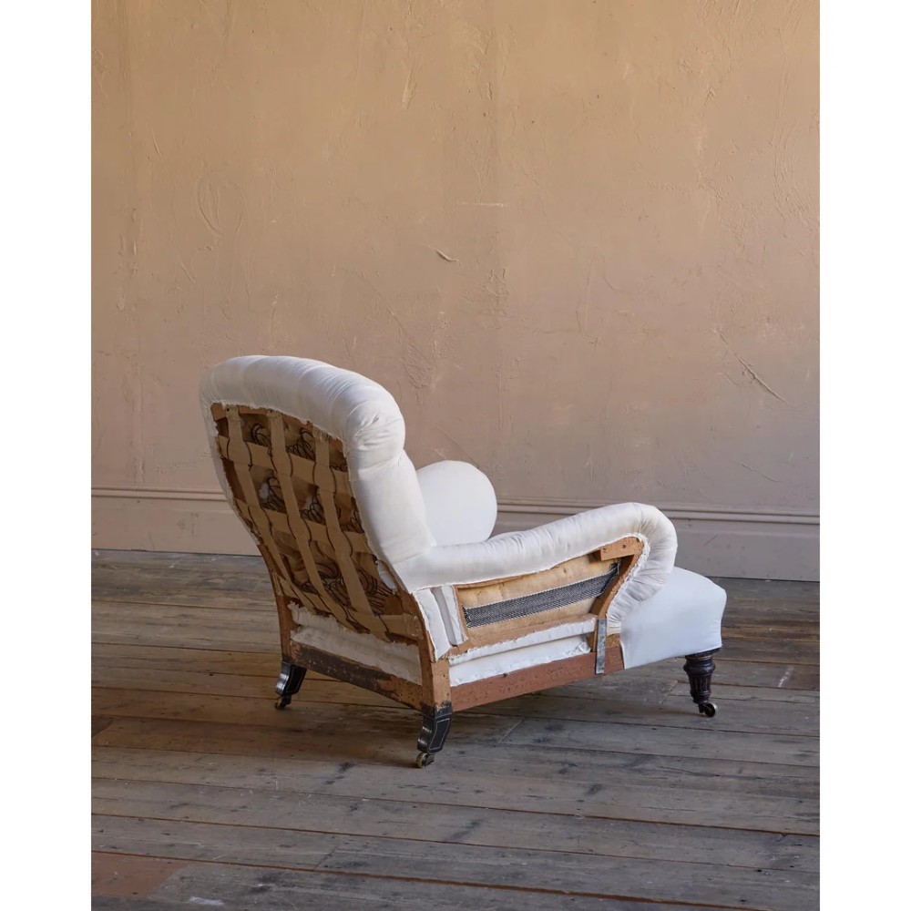 A deep-seated Howard style armchair upholstered in cream calico fabric with a button-tufted backrest and turned wooden legs on brass castors. View III