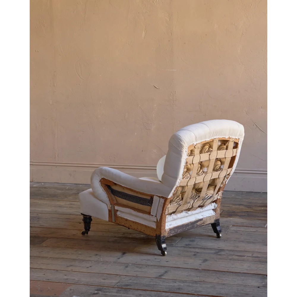 A deep-seated Howard style armchair upholstered in cream calico fabric with a button-tufted backrest and turned wooden legs on brass castors. View IV