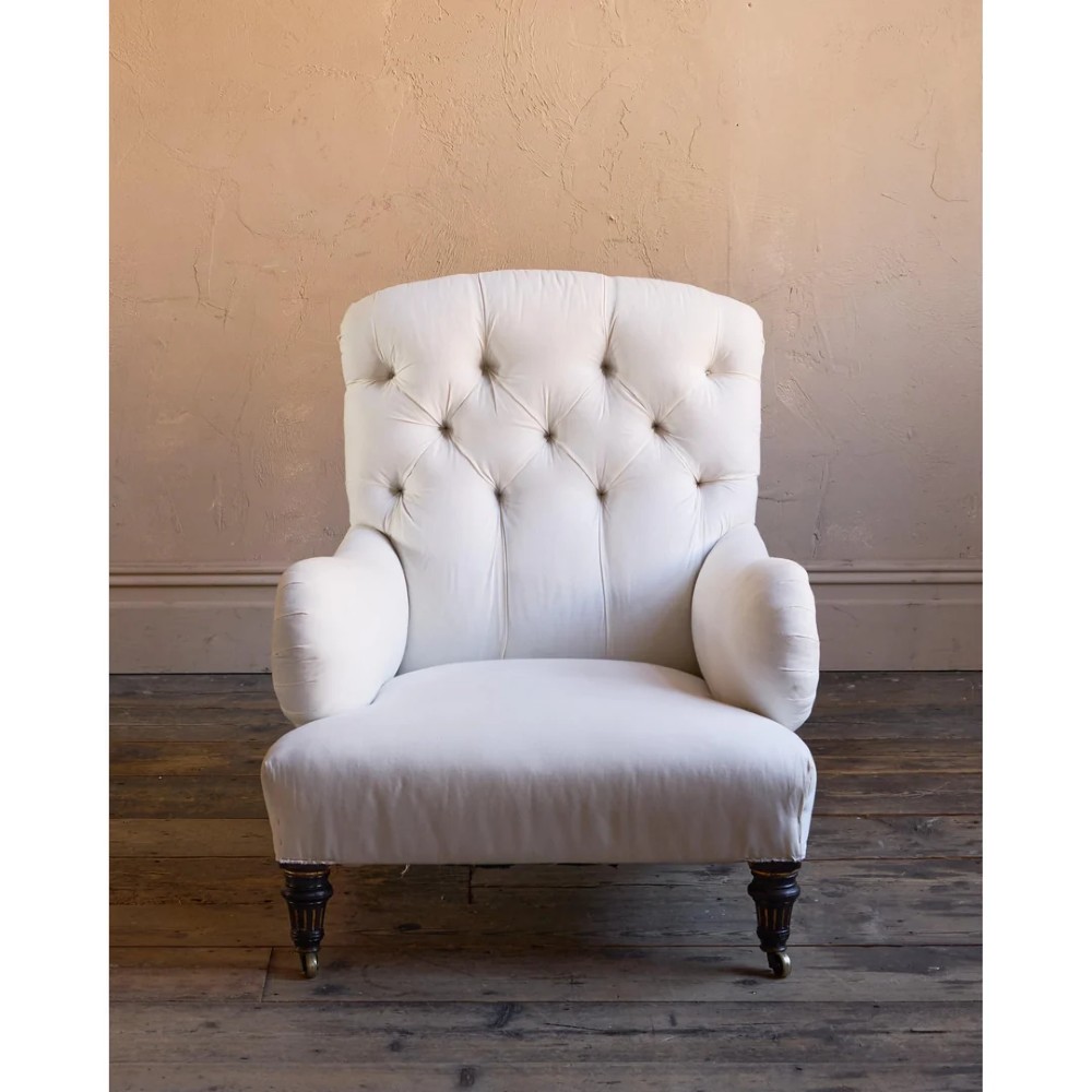 A deep-seated Howard style armchair upholstered in cream calico fabric with a button-tufted backrest and turned wooden legs on brass castors. View V
