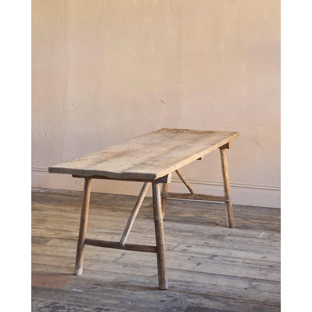 A primitive rustic dining table constructed from weathered pale timber with a rough-hewn plank top and diagonal cross-braced legs. View II
