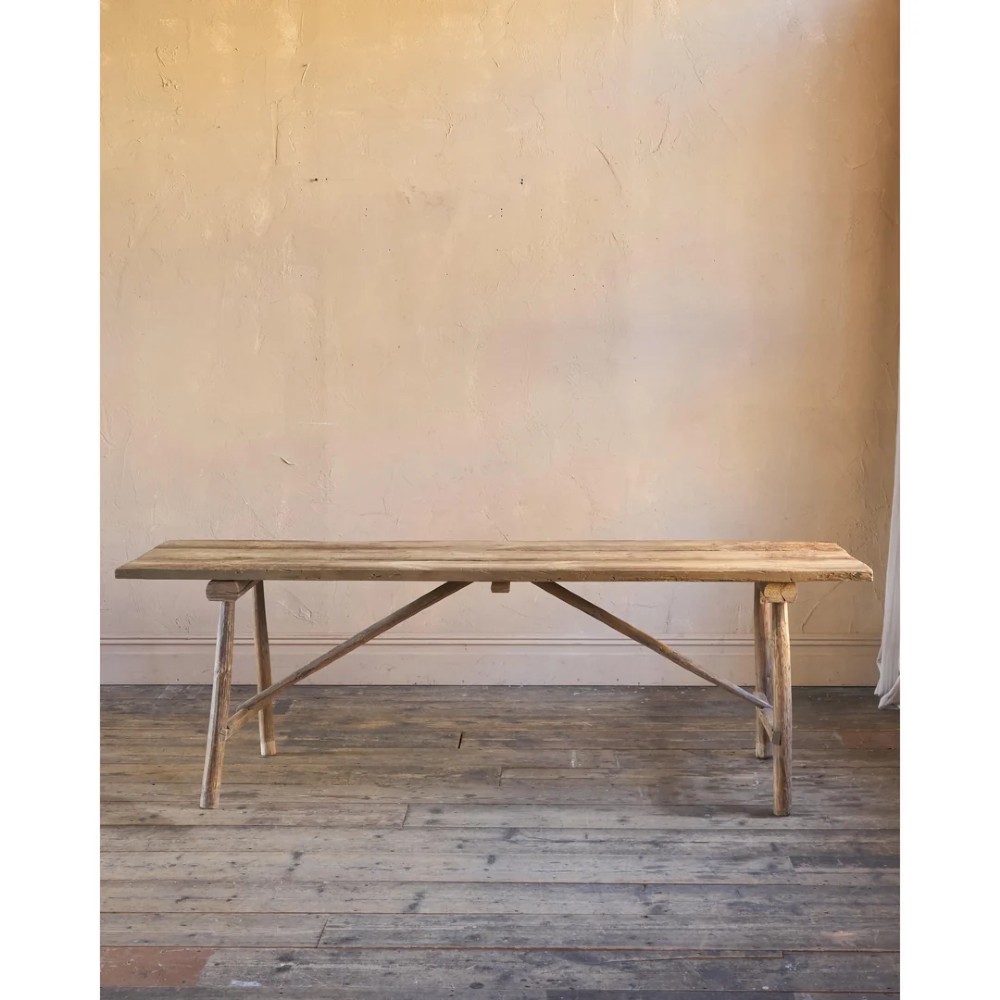 A primitive rustic dining table constructed from weathered pale timber with a rough-hewn plank top and diagonal cross-braced legs. View III