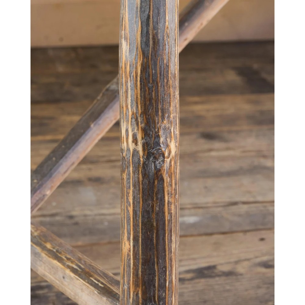 A primitive rustic dining table constructed from weathered pale timber with a rough-hewn plank top and diagonal cross-braced legs. View VI