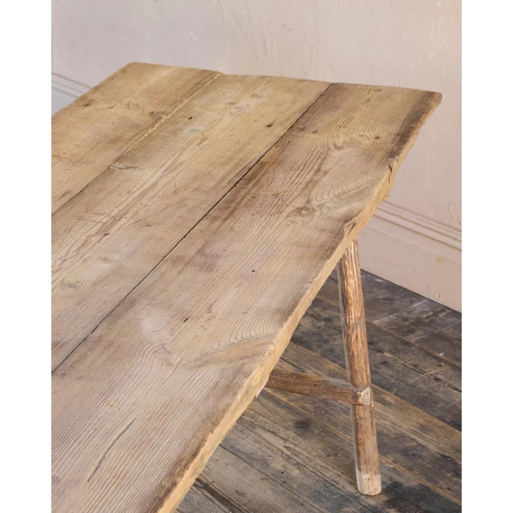 A primitive rustic dining table constructed from weathered pale timber with a rough-hewn plank top and diagonal cross-braced legs. View XI