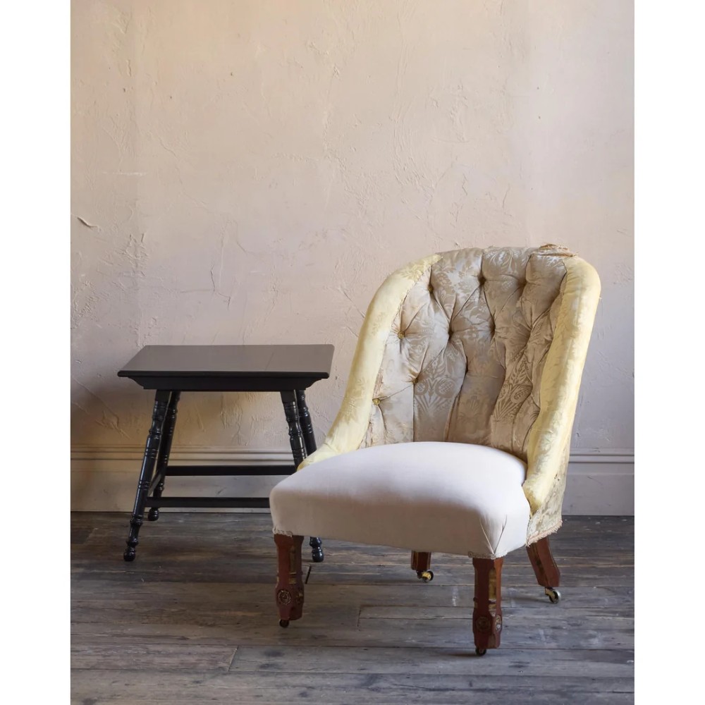 A low Victorian upholstered armchair featuring a deep button-backed yellow damask backrest, a plain off-white seat, and carved mahogany front legs on brass castors.
