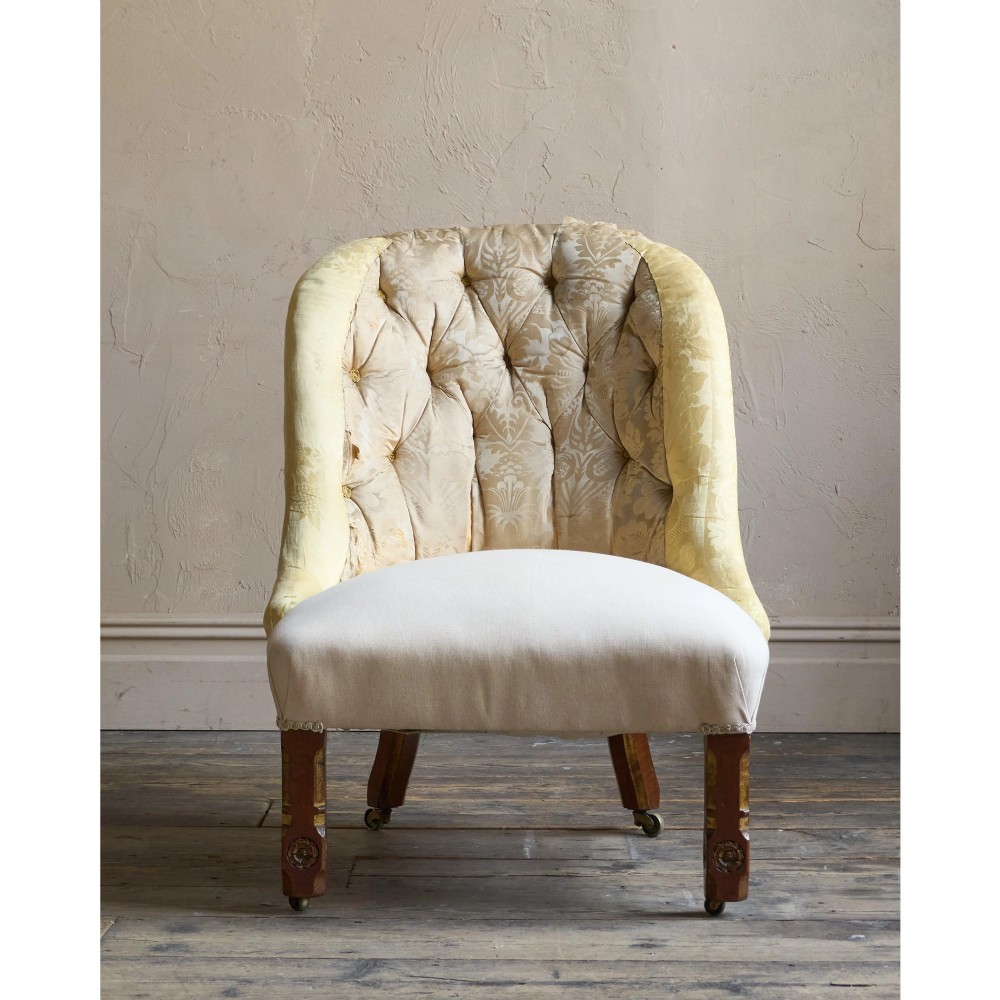A low Victorian upholstered armchair featuring a deep button-backed yellow damask backrest, a plain off-white seat, and carved mahogany front legs on brass castors. View V