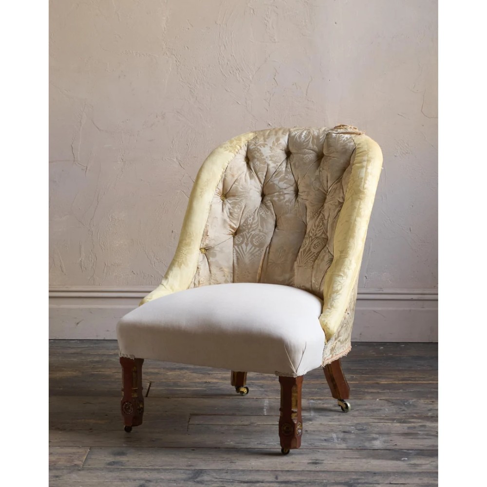 A low Victorian upholstered armchair featuring a deep button-backed yellow damask backrest, a plain off-white seat, and carved mahogany front legs on brass castors. View VI