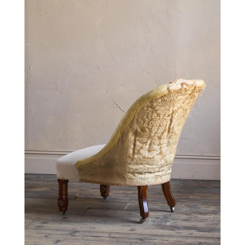 A low Victorian upholstered armchair featuring a deep button-backed yellow damask backrest, a plain off-white seat, and carved mahogany front legs on brass castors. View VII