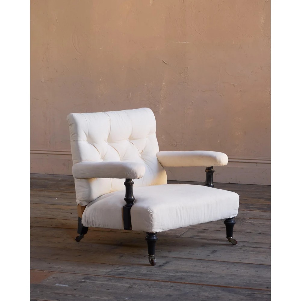 An antique Victorian open armchair upholstered in off-white calico fabric featuring a deep-buttoned backrest, padded arms, turned dark timber supports, and legs on castors.